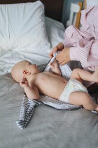 Crop mom dressing newborn on bed